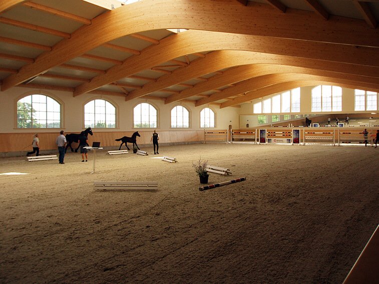 Helles und geräumiges Innenbild einer Reithalle mit Hindernissen, die für Training und Pferdeausbildung genutzt wird.